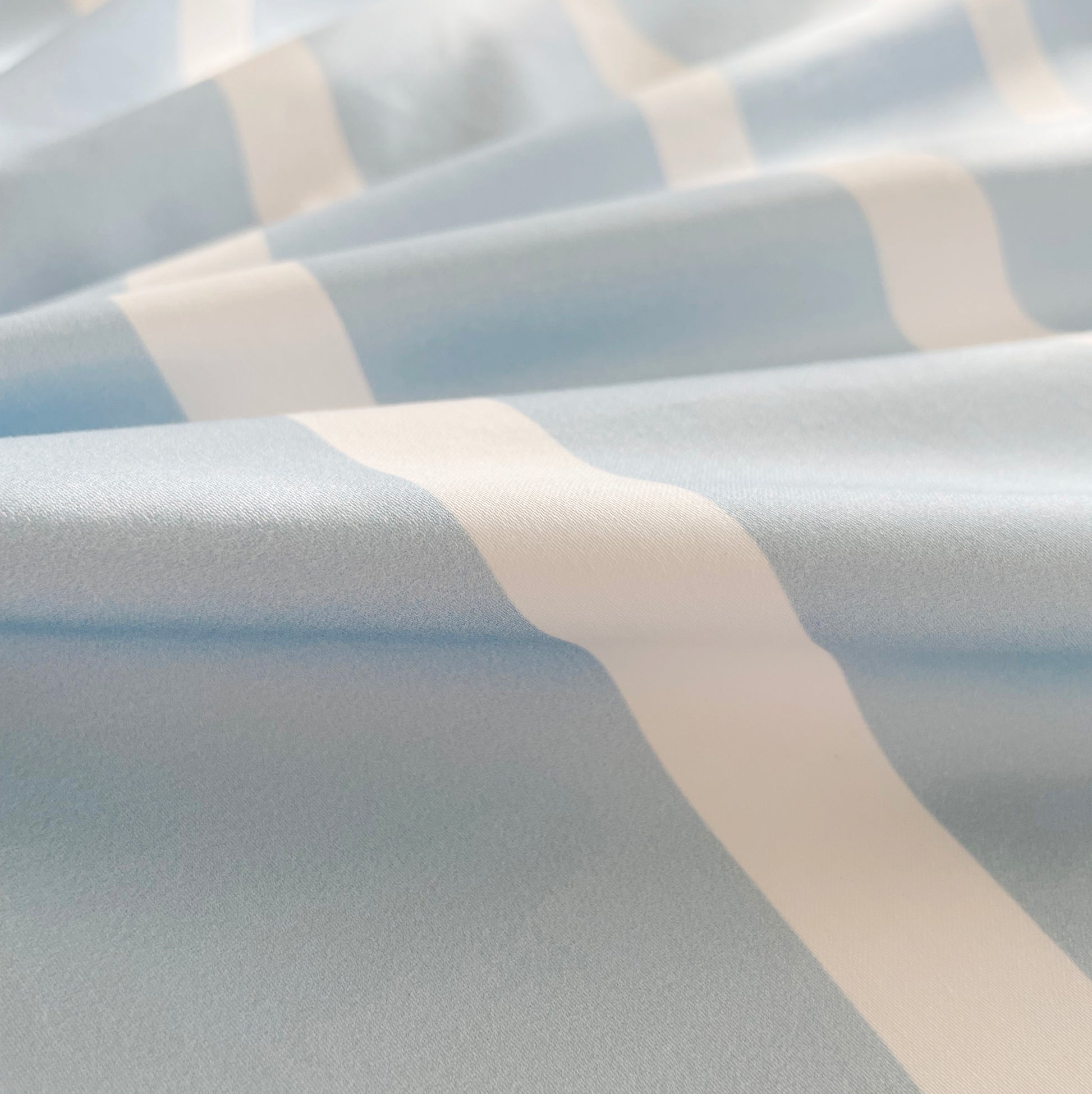 A close-up of soft, breathable blue and white striped pure cotton fabric, showcasing its smooth texture and high-quality weave. The fabric’s gentle feel and durability make it perfect for a cozy and comfortable bedding experience.
